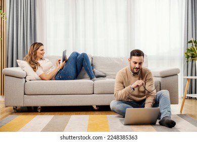 A happy couple is using tablet and laptop at home in a living room. - Shutterstock ID 2248385363
