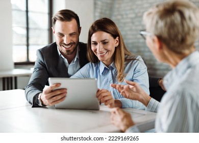 Happy couple using touchpad  while having a meeting with their insurance agent in the office - Powered by Shutterstock