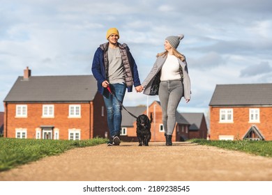 Happy Couple Walking The Dog On A Sunny Autumn Day - Young Couple With A Black Dog On Leash Enjoying Neighbourhood Walk - Lifestyle And Animals Concepts