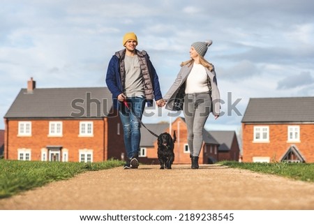 Happy couple walking the dog on a sunny autumn day - Young couple with a black dog on leash enjoying neighbourhood walk - Lifestyle and animals concepts