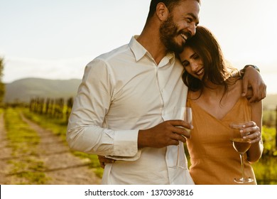 Happy couple walking outdoors holding each other drinking white wine. Couple in love spending time together walking in a wine farm holding each other. - Powered by Shutterstock