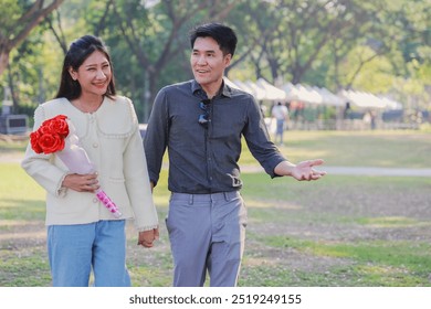 Happy couple walking in the park, woman holding bouquet of red roses, daytime, green trees in background. - Powered by Shutterstock