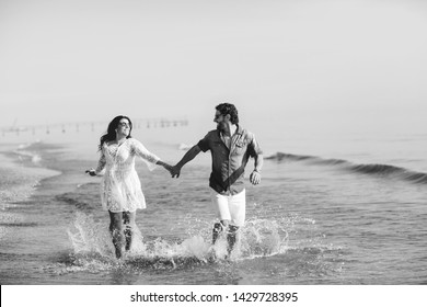 Happy Couple Walking And Playing On The Beach, Soaking His Feet In The Water. Wonderful Love Story In Rimini, Italy. Black And White