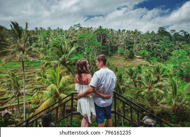 Happy Couple Walking At The Rice Terraces, Holds Hands. Traveling At Bali. Honeymoon Summer Travel At Indonesia.