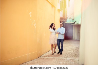 Happy Couple Walking Together And Laughing In Tiny Streets Of A Town. Sun Flares And Copy Space In Background 