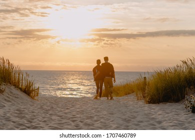 Happy Couple Walking To Watch The Sunset By The Beach In Le Pin Sec, Borrdaux (France) After A Surf Session.