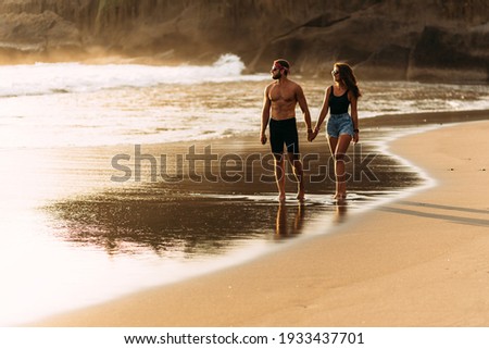 A happy couple walks along a sandy beach on the island of Bali. Couple in love at sunset by the sea. Couple in love on vacation. Honeymoon trip. Romantic couple enjoying a beach walk at sunset 