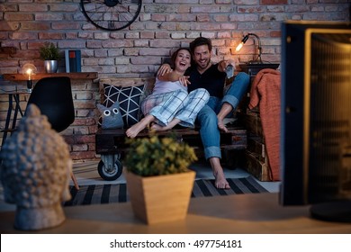 Happy couple watching comedy at home on tv, sitting on pallet furniture.