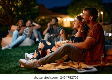 Happy couple watching movie with friends in the backyard at night. - Powered by Shutterstock