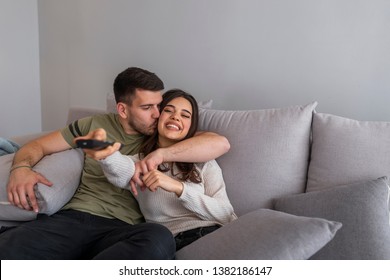 Happy couple watching a movie on TV sitting on a couch at home. Young couple watching TV on a sofa at home. Happy family sitting on sofa at home and looking at you showing remote control at camera 