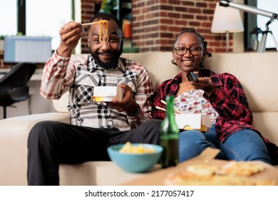 Happy Couple Watching Television And Eating Noodles Meal, Switching Tv Channel Program With Remote Control. Having Takeaway Dinner Food While They Watch Movie Or Film, Leisure Activity.