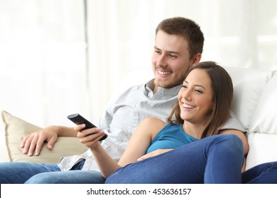 Happy couple watching tv at home sitting in a comfortable couch in the livingroom at home