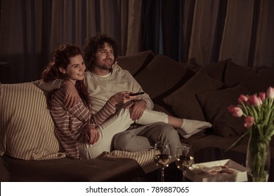 happy couple watching tv on sofa in evening  