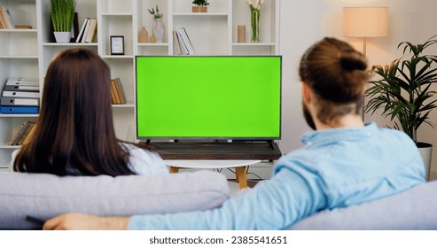 Happy couple watching tv and switching channels looking at green screen in modern living room. Woman and man watching chroma key television. - Powered by Shutterstock