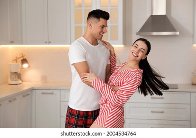 Happy Couple Wearing Pyjamas And Dancing In Kitchen