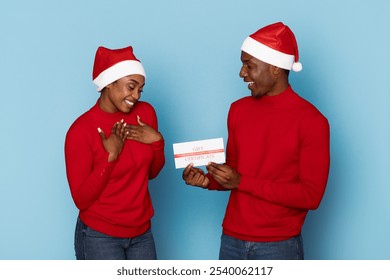 A happy couple wearing red sweaters and Santa hats share a heartfelt moment while exchanging a gift. The playful atmosphere captures the spirit of the holiday season. - Powered by Shutterstock