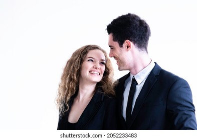 Happy Couple Wearing Suit Smiling And Embracing Each Other While Looking At Each Other Isolated Against White. Professional Successful Couple Embracing Together. Relationships And People Concept.