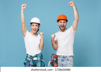 Happy couple woman man in casual clothes protective helmet hardhat isolated on blue background. Instruments accessories for renovation apartment room. Repair home concept. Clenching fists like winner