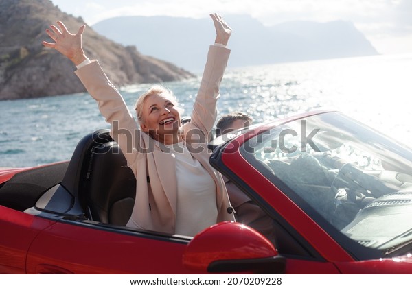 Happy\
couple, woman and man hugging outdoor and trevelling in the\
convertible red car. People dressed fashion\
coat