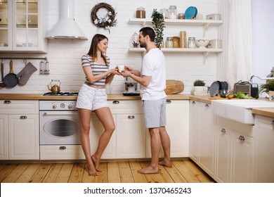 Happy Couple Woman And Man Making Coffee With Machine At Their Kitchen In New Home. Having Fun Together And Cooking Breakfast. Happy Young Family Concept