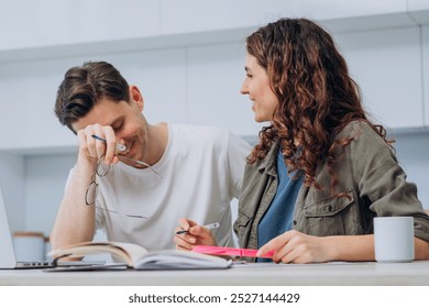 Happy couple working together at home, laughing and discussing, casual teamwork and collaboration. Man and woman smiling surrounded by books and laptop, enjoying lighthearted moment. - Powered by Shutterstock