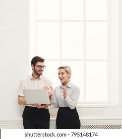 Happy Couple Of Young Business Partners Working In Modern Office. Two Coworkers Working On Laptop While Standing Near Window, Copy Space