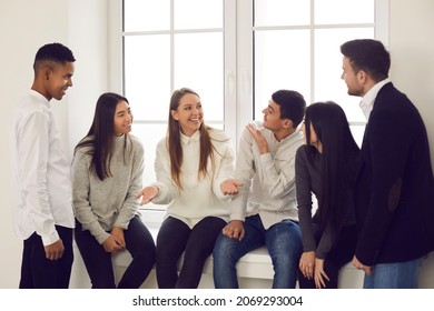 Happy coworkers, college students or friends talking about funny things during break. Group of cheerful diverse people sitting on windowsill, smiling, having fun and enjoying informal communication