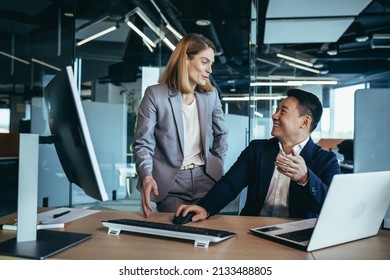 Happy Coworkers Discuss Project Strategy By Looking And Pointing At Laptop Pc Computer Monitor Screen. Multiethnic Business Team In The Office. Confident Mature Asian Man Explaining Young Female