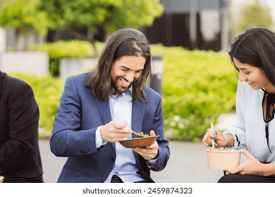 Happy coworkers sharing a laugh during an outdoor lunch, healthy meals in hand. - Powered by Shutterstock