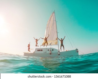 Happy crazy friends diving from sailing boat into the sea - Young people jumping inside ocean in summer vacation - Main focus on left girls - Travel and fun concept - Fisheye lens distortion