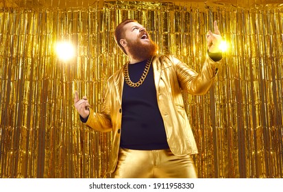 Happy Crazy Funky Uninhibited Bearded Chubby Man In Funny Shiny Golden Suit And Extravagant Gold Chain Having Fun At Disco Party, Celebrating Success, Singing Songs And Doing Horn Sign Hand Gesture