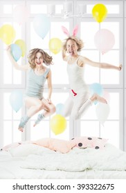 Happy crazy two friends girl, Jumping having fun pijamas party on the bed. Sunny light room with . Active emotional woman