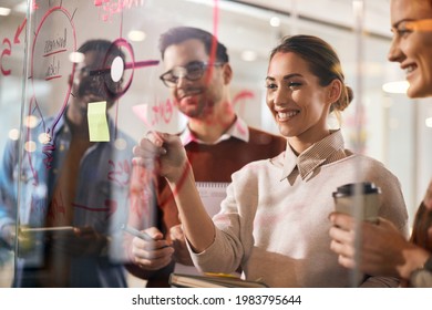 Happy creative business team making mind map on glass wall at casual office. Focus is on businesswoman using adhesive note. The view is through the glass. - Powered by Shutterstock