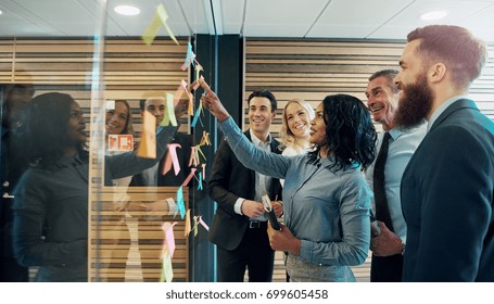 Happy creative businesspeople brainstorming in office, placing sticky notes with ideas on glass