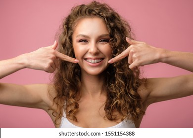 Happy curly girl with her dental braces pointing her finger to her smile