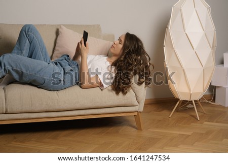 Happy curly hair girl in casual clothes sitting on sofa with her phone