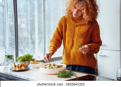 Happy Curly Woman In Sweater Cooking Healthy Vegan Salad And Appetizers For Family Feasting. Christmas, New Year, Thanksgiving, Anniversary, Hanukkah, Mothers Day, Easter, Engagement Concept