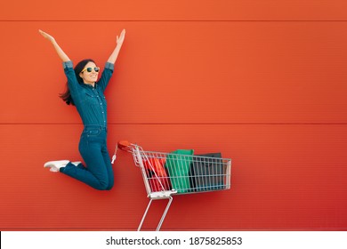 Happy Customer Jumping With Joy In Front Of A Supermarket. Super Excited Female Client Having A Great Shopping Experience
