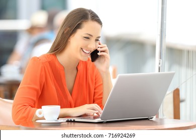 Happy Customer In Orange Using A Laptop And Talking On Phone Sitting In A Bar Terrace