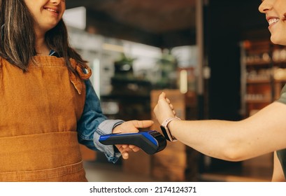 Happy customer scanning her smartwatch on a credit card machine to pay her bill in a cafe. Cheerful woman doing a cashless and contactless transaction using NFC technology. - Powered by Shutterstock