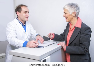 Happy Customer, Senior Older Woman, Paying Her Medical Bill At The Clinic