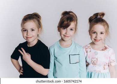 Happy Cute Adorable Blondie Triplets Girls Posing In Studio Together On Isolated Background. Childhood, Children, Twins Concept. Smiling Girls Playing Together