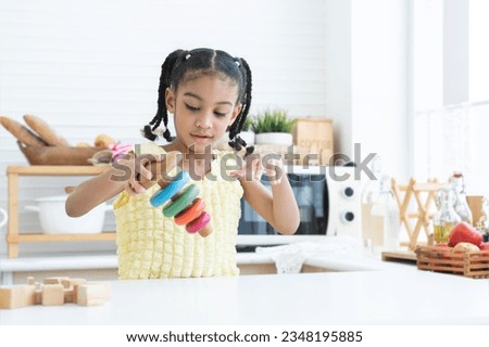 Happy cute African little child girl smiling, playing wooden blocks toy and colorful pyramid puzzle in kitchen at home. Education, development, child care concept
