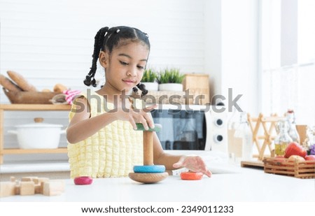 Happy cute African little child girl smiling, playing wooden blocks toy and colorful pyramid puzzle in kitchen at home. Education, development, child care concept