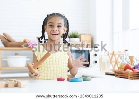Happy cute African little child girl smiling, playing wooden blocks toy and colorful pyramid puzzle in kitchen at home, looking at camera. Education, development, child care concept