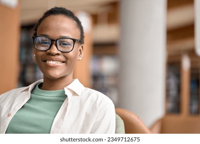 Happy cute African teen girl, smiling short-haired cute Black ethnic college student wearing eyeglasses looking at camera in modern university campus library. Close up face portrait. - Powered by Shutterstock