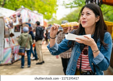 happy cute asian gilr eating japanese street food and looking enjoyable in a traditional small fair.