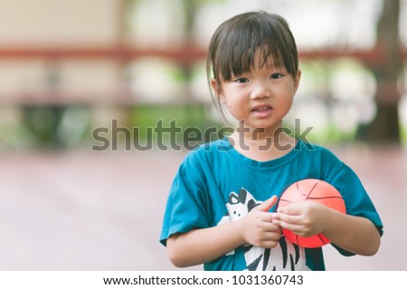 Happy cute asian girl smiling and  holding small basketball in the park with sun light background. Funny adorable Asia child playing mini ball alone in the garden with blurred background.