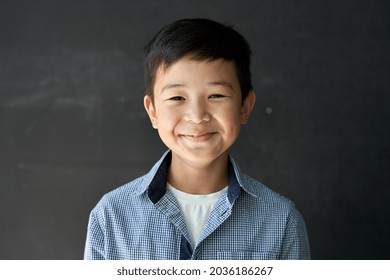 Happy Cute Asian Kid Boy School Student Looking At Camera At Blackboard Background. Smiling Ethnic Child Pupil Posing In Classroom. Junior Elementary Education. Back To School In Asia Concept Portrait