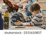 Happy cute boy helping his father in the garage, he is cleaning a helmet